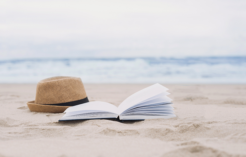 Barret masculí de palla i llibre obert a la sorra d'una platja