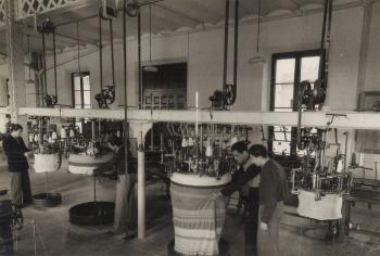 Telers rodons de malloses al taller de l’edifici principal abans que es fes el trasllat a la Nau Floris. És l’actual sala d’actes de l'Escola de Teixits de Punt de Canet de Mar, c. 1940. Autoria desconeguda. Fons: Diputació de Barcelona. (CAT AGDB R.11135_1)